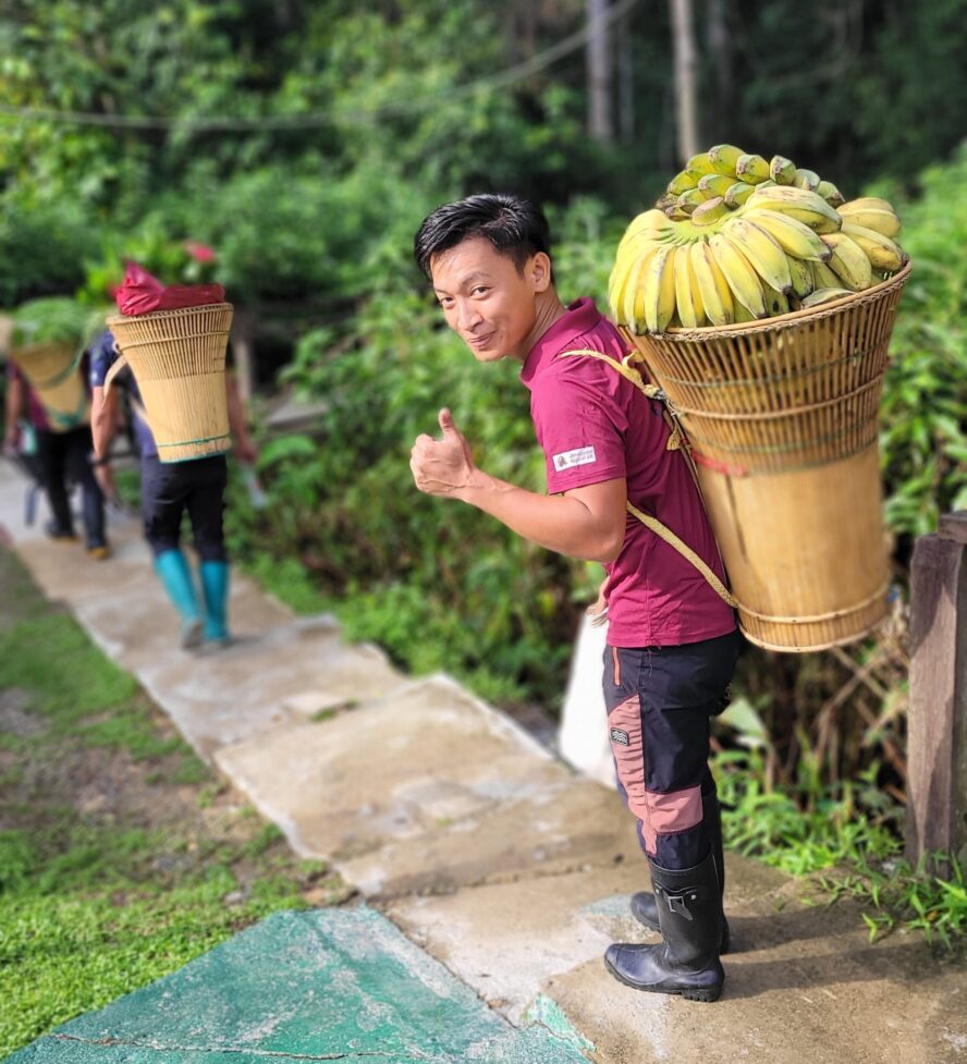 Arnold caring a basket of bananas whilst smiling and giving a thumbs up