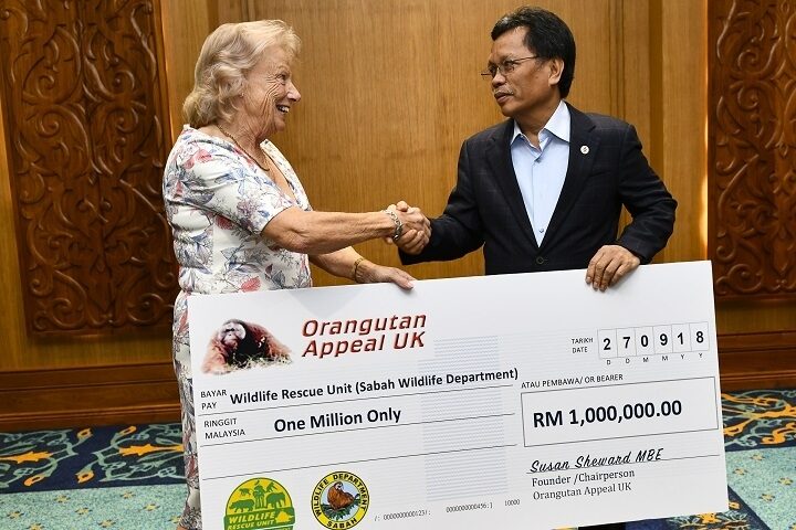 Two people standing and shaking hands whilst holding onto a large cheque for 1 million RM.