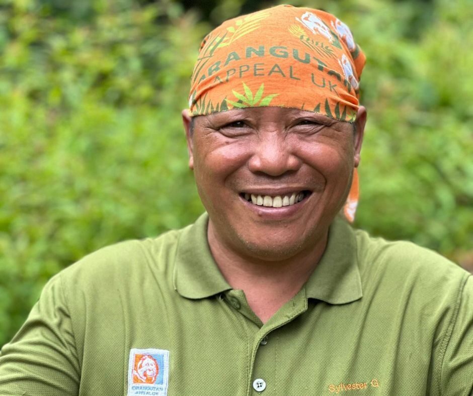 Man wearing a bright orange headband with the Orangutan Appeal UK logo across it and green leaf design.