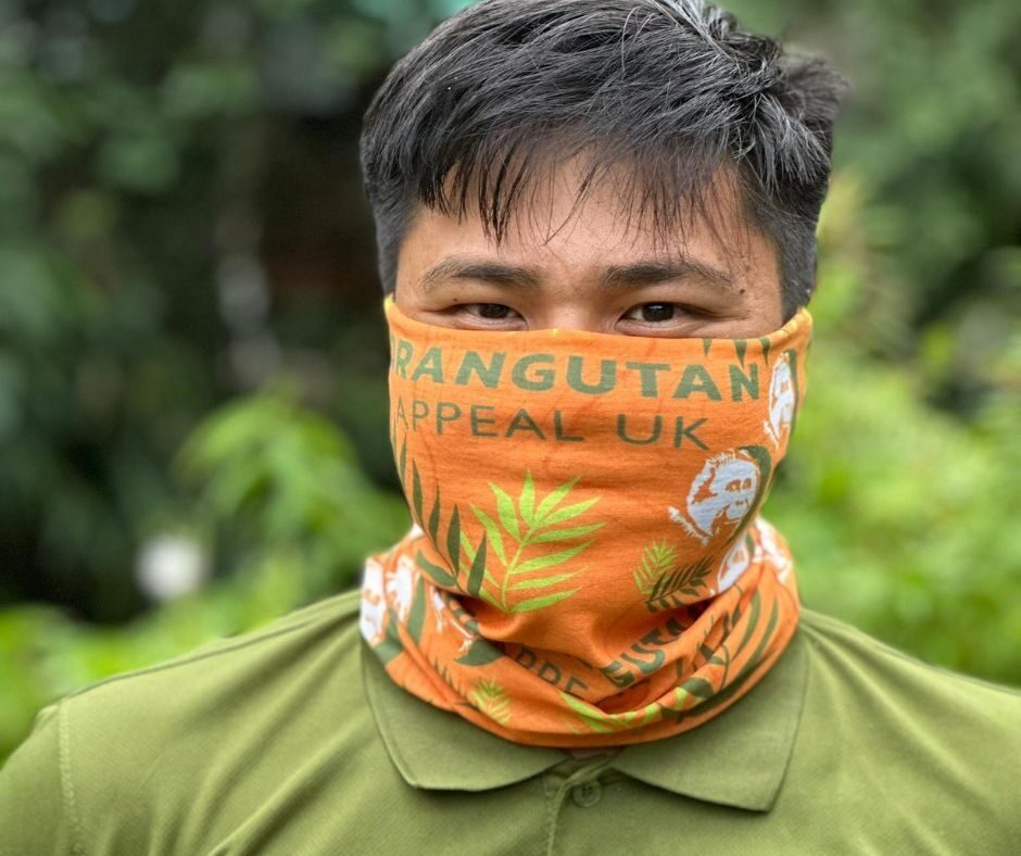 Man wearing a bright orange headband as a face covering with the Orangutan Appeal UK logo across it and green leaf design.