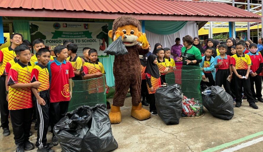 Students standing with bags of rubbish collected next to orangutan mascot.