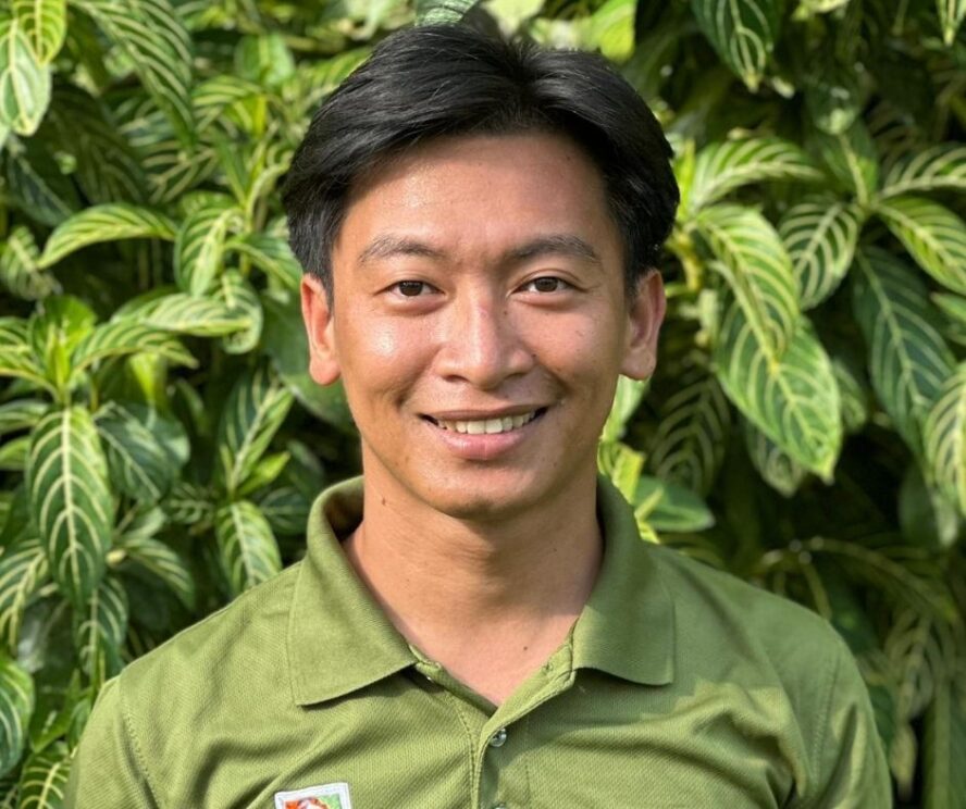 A man standing in front of a green leafy bush.