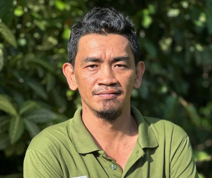 A man standing in front of a green leafy bush.