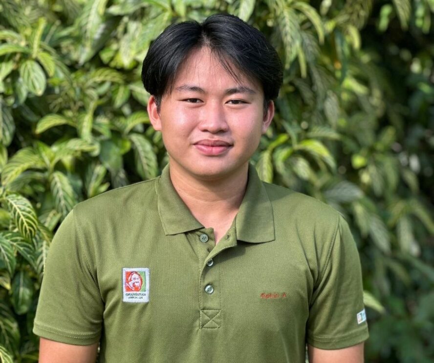 A man standing in front of a green leafy bush.