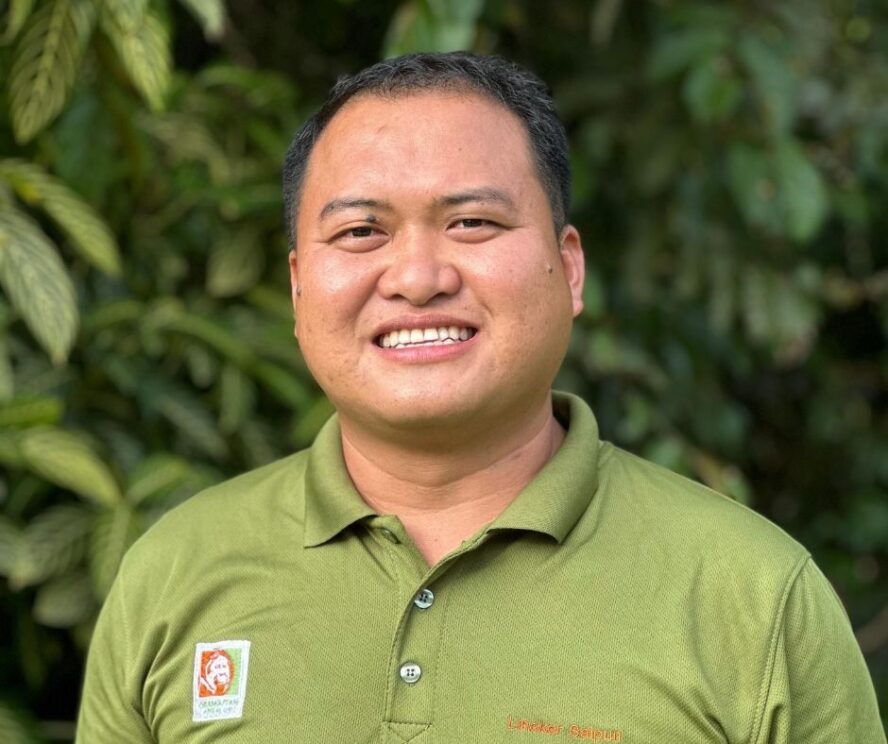 A man standing in front of a green leafy bush.