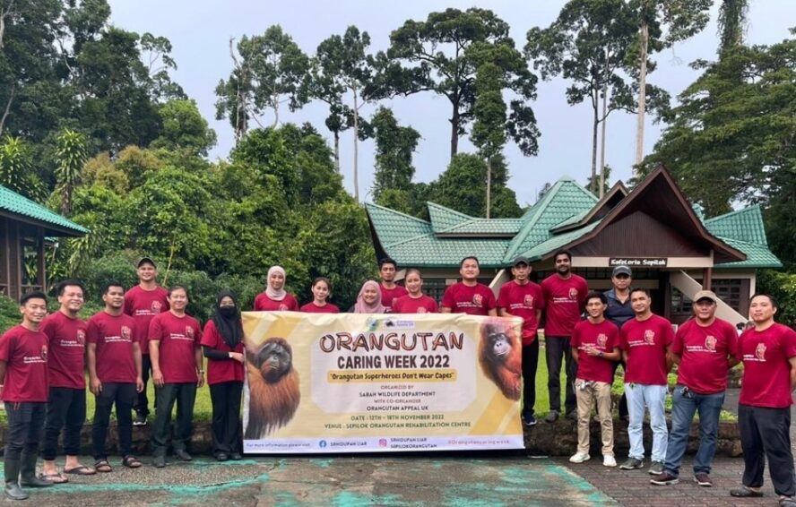 Sepilok staff in read matching polos stand and pose for photo whilst holding up Orangutan Caring Week 2022 banner.