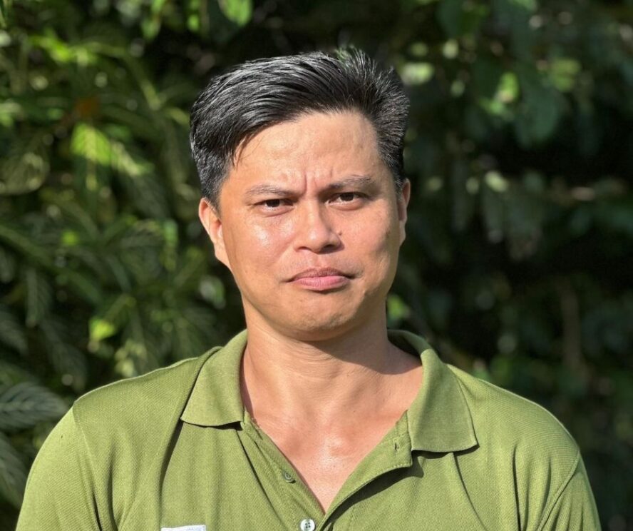 A man standing in front of a green leafy bush.