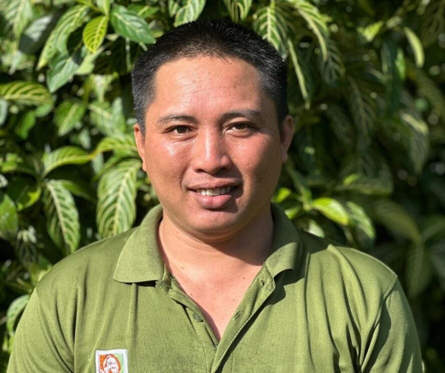 A man standing in front of a green leafy bush.
