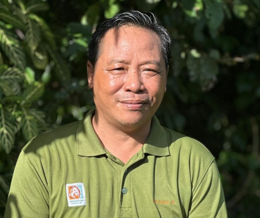 A man standing in front of a green leafy bush.