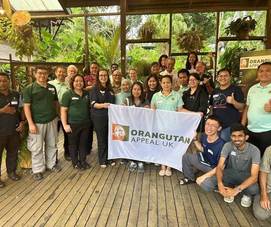 Group photo at networking event with people crowded around holding a flag of the Orangutan Appeal UK logo.